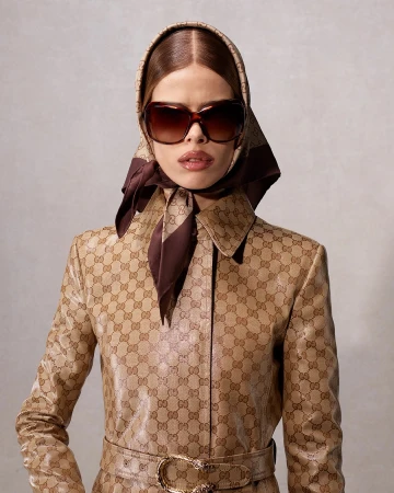 Model wearing oversized sunglasses, a matching monogram headscarf, and a belted coat against a neutral background.