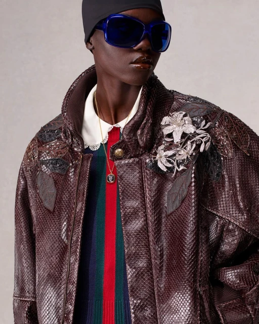 Fashion shot of an adult woman with dark skin wearing a snakeskin jacket, colorful sweater, black beanie, and sunglasses in a studio.