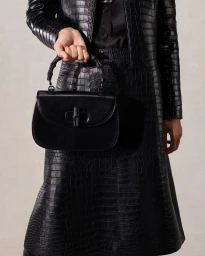 Person holding a black leather handbag wearing matching embossed crocodile texture coat and skirt against a grey background