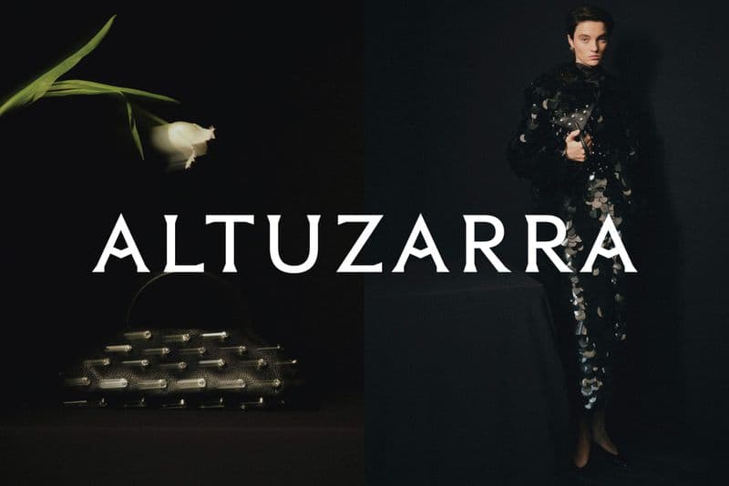 Model wearing dark textured clothing and holding a handbag next to a white tulip on a dark background for the Altuzarra campaign.