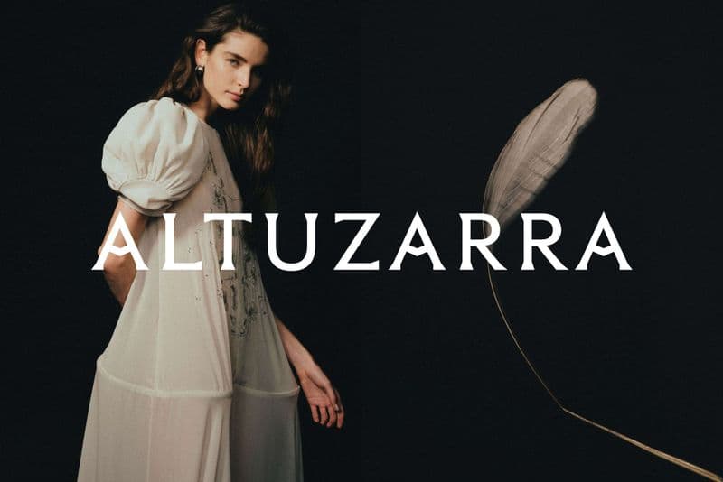 Model wearing a light cream dress against a solid black background with the brand name Altuzarra overlaid across the center.