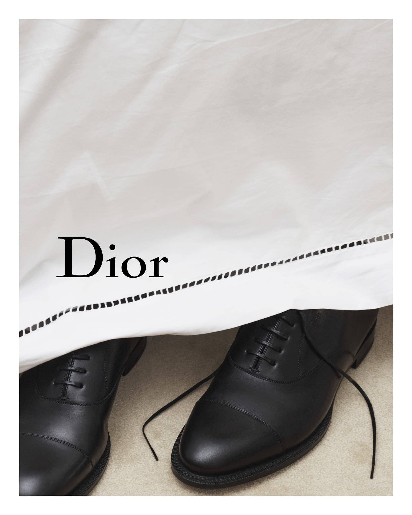 Elegant black leather dress shoes displayed under a white fabric featuring the Dior logo in a fashion-forward presentation.