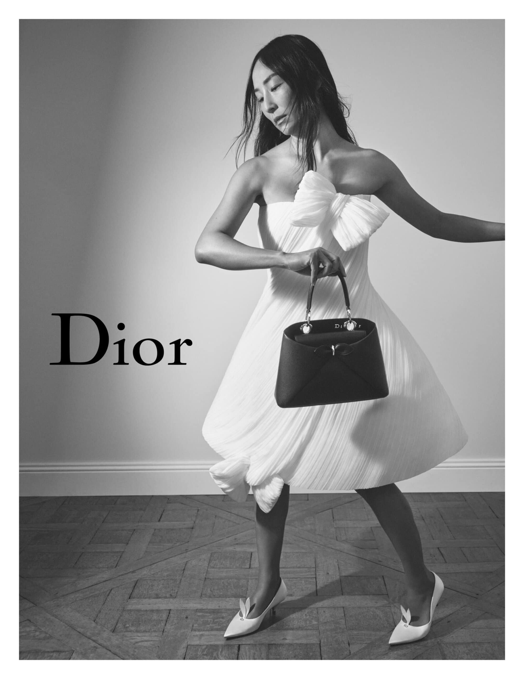 Greta Lee wearing a strapless white dress and holding a dark handbag for Dior Spring 2026 campaign photographed in black and white