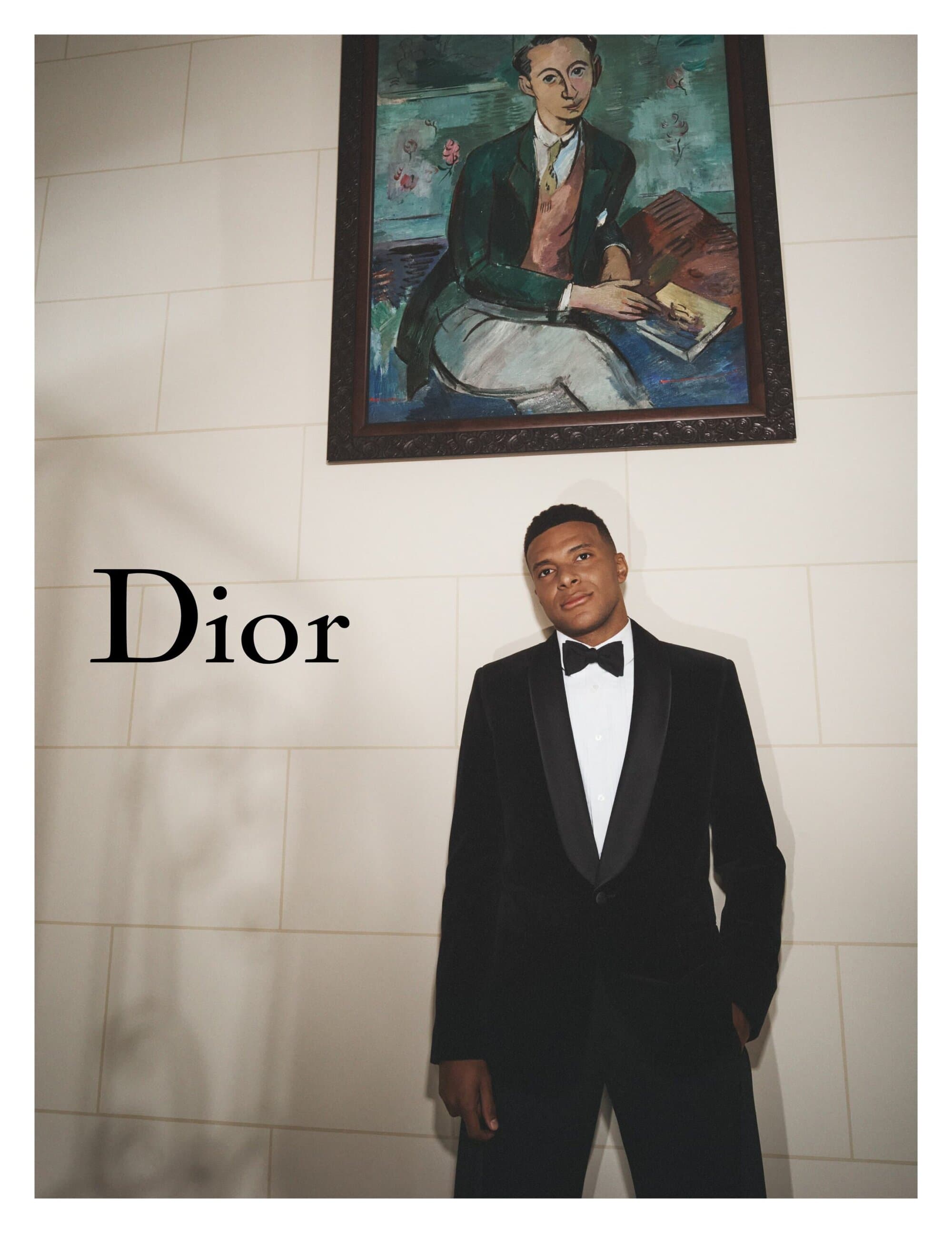 Man in black tuxedo stands under portrait in an indoor setting, fashion brand advertisement, neutral color palette.