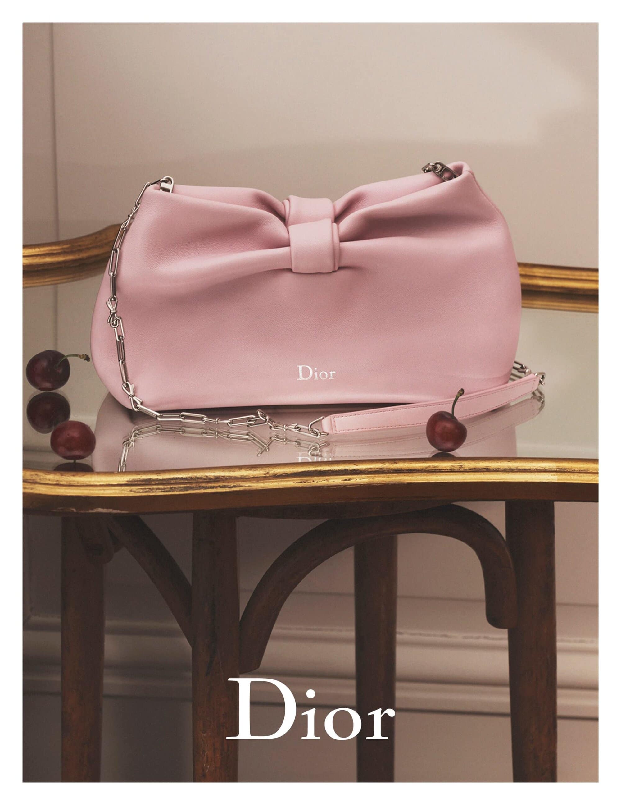 Elegant pink leather Dior handbag on a gold-trimmed table with dark cherries, showcasing luxury fashion and designer accessories.