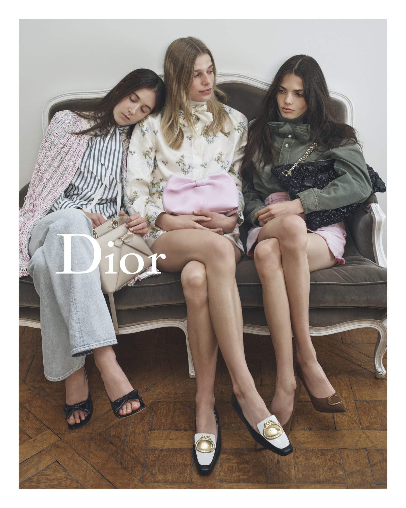 Three fair-skinned women seated on a grey couch wearing fashionable clothes and shoes, indoor, medium shot. Dior logo is visible.