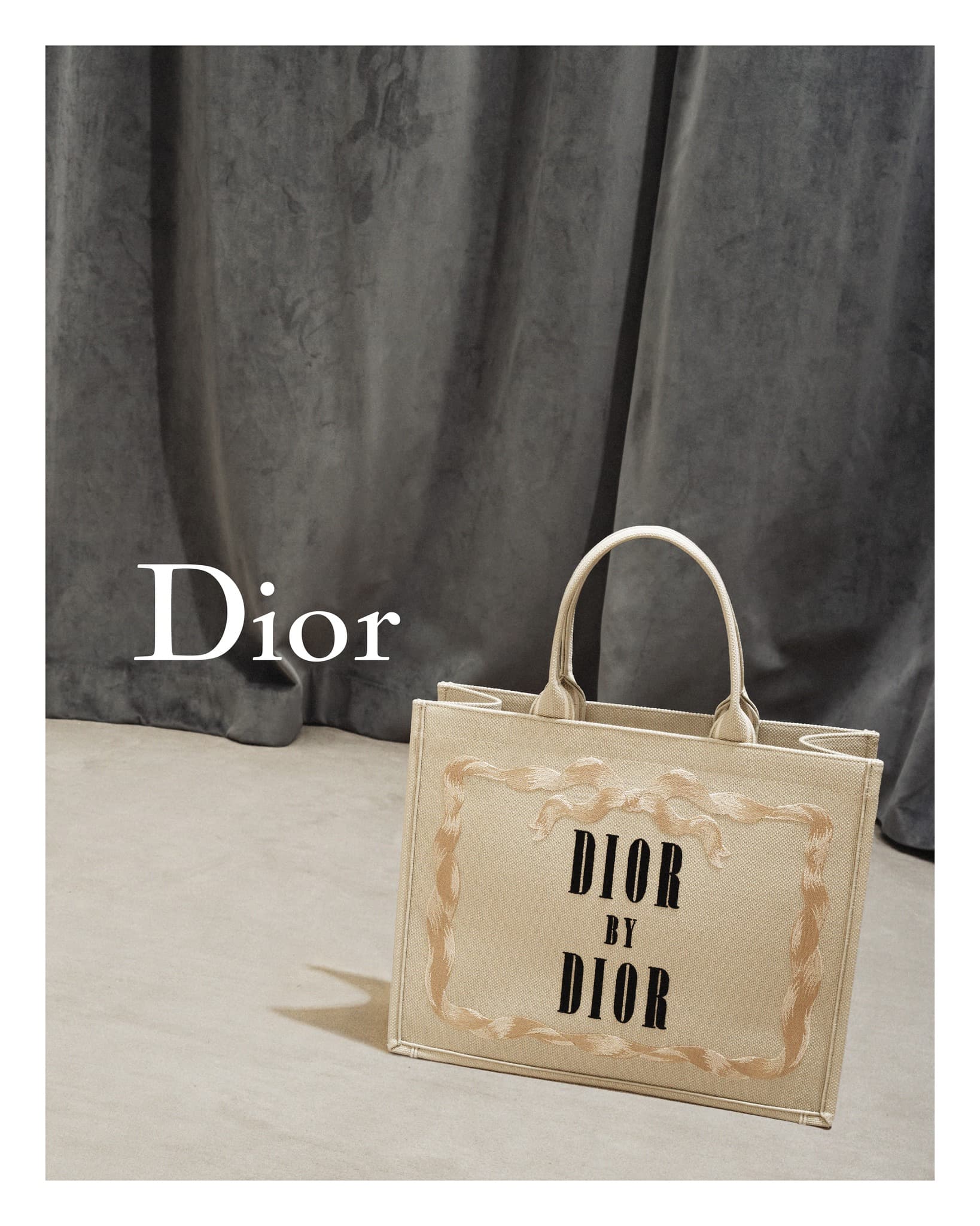 Tan Dior Book Tote bag featuring a 'Dior by Dior' pattern is displayed against a neutral backdrop with draped grey fabric.