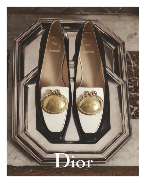 Elevated shot of black and white Dior loafers with gold embellishments, presented on an octagonal silver tray against a marble backdrop.