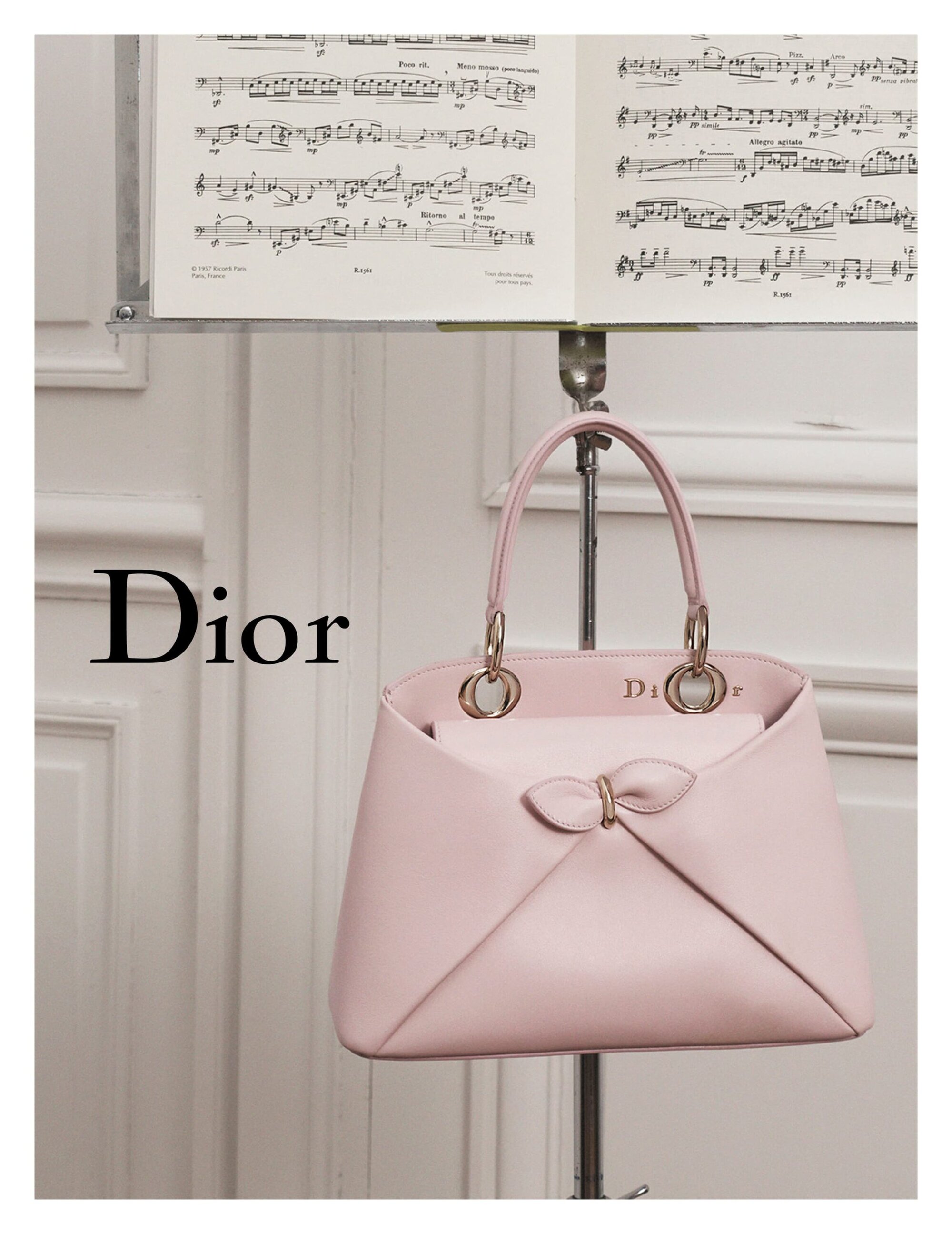 Elegant pink Dior handbag on a music stand with sheet music in a bright indoor setting, showcasing luxury fashion and classic design.