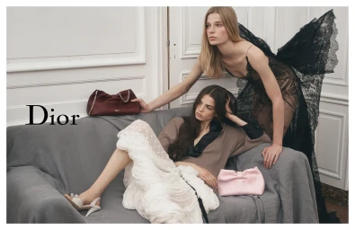 Two female models posing with Dior handbags in an interior setting with white paneling and a grey sofa