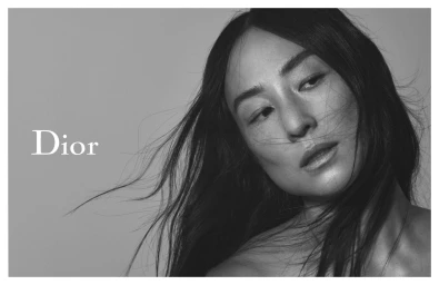 Black and white portrait of a woman with dark hair blowing across her face against a plain light background with Dior branding