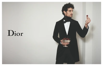 Louis Garrel in a black velvet suit holding a silver bowl of cherries for Dior Spring 2026 Ad Campaign against a white background