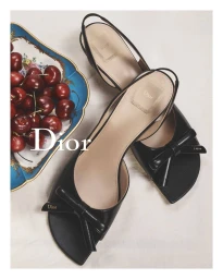 Black slingback heels with front bows displayed next to a decorative bowl of fresh red cherries on a white background
