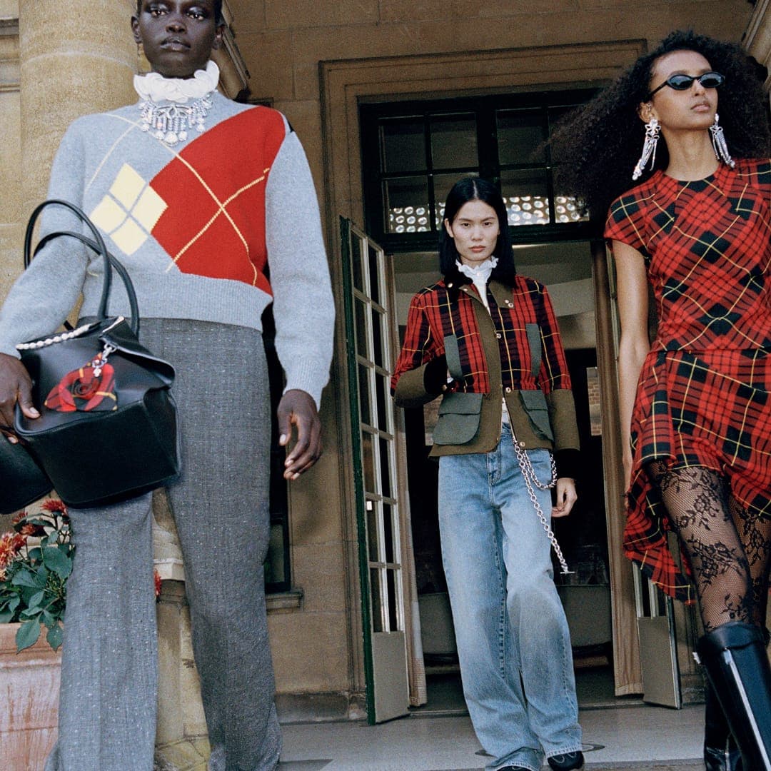 Three models in tartan and argyle fashion outside a stone building for McQueen