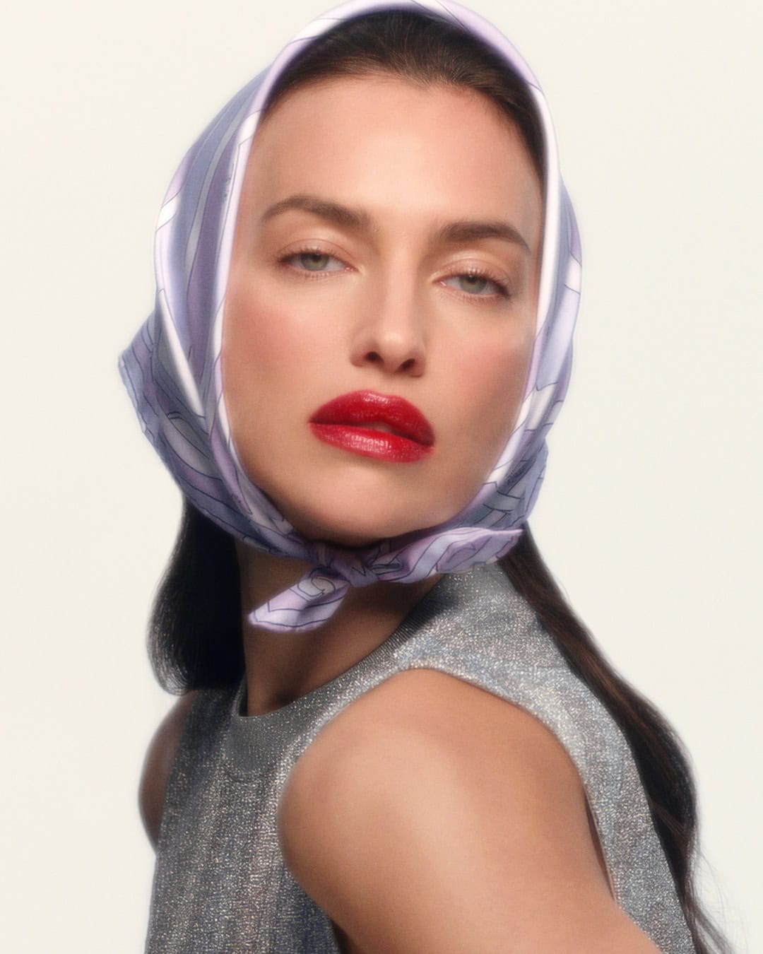 Model Irina Shayk wearing a patterned silk headscarf and a sleeveless metallic top against a plain light background