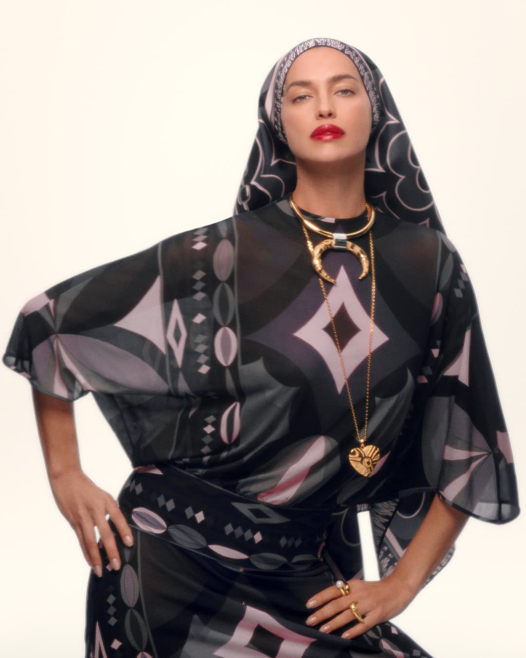Model Irina Shayk wearing a patterned Pucci headscarf and matching printed top with bold gold jewelry against a white background.