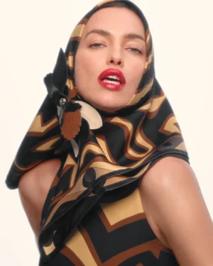 Model Irina Shayk wearing a patterned silk headscarf and matching geometric top with bright red lipstick against a plain white background.