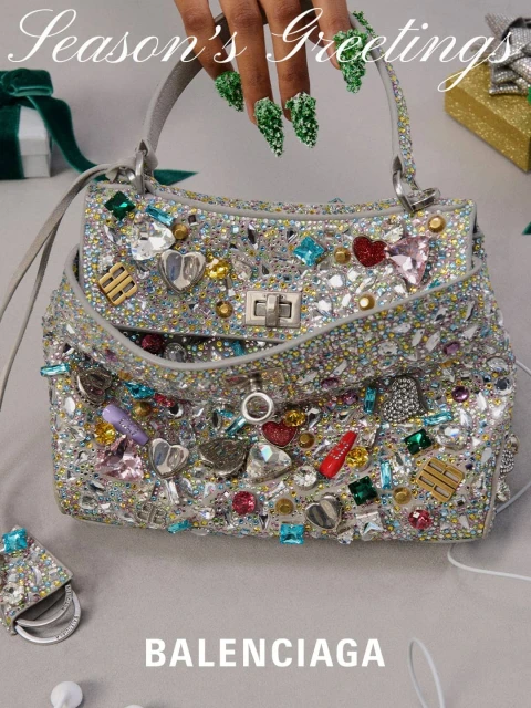 Embellished Balenciaga purse with ornate silver hardware, rhinestones, and heart charms set against a neutral surface near holiday-themed gift.