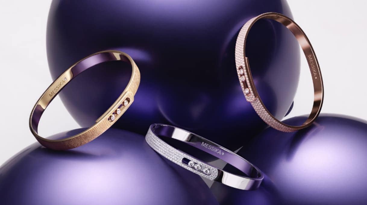 Three Messika Move Uno bangles in rose gold, white gold, and yellow gold with pavé diamonds, resting on violet-colored spheres.