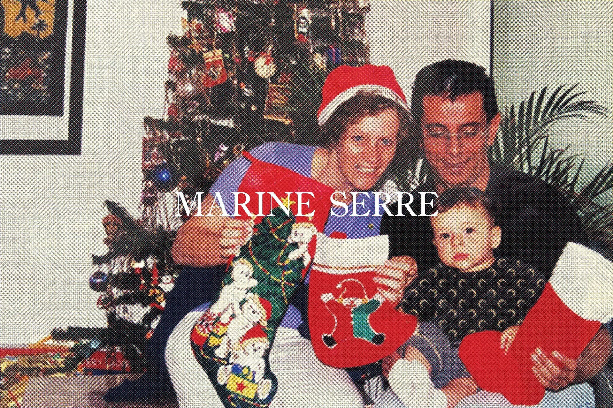 Family poses with festive Christmas stockings in an indoor setting, a decorated Christmas tree is in the background. 