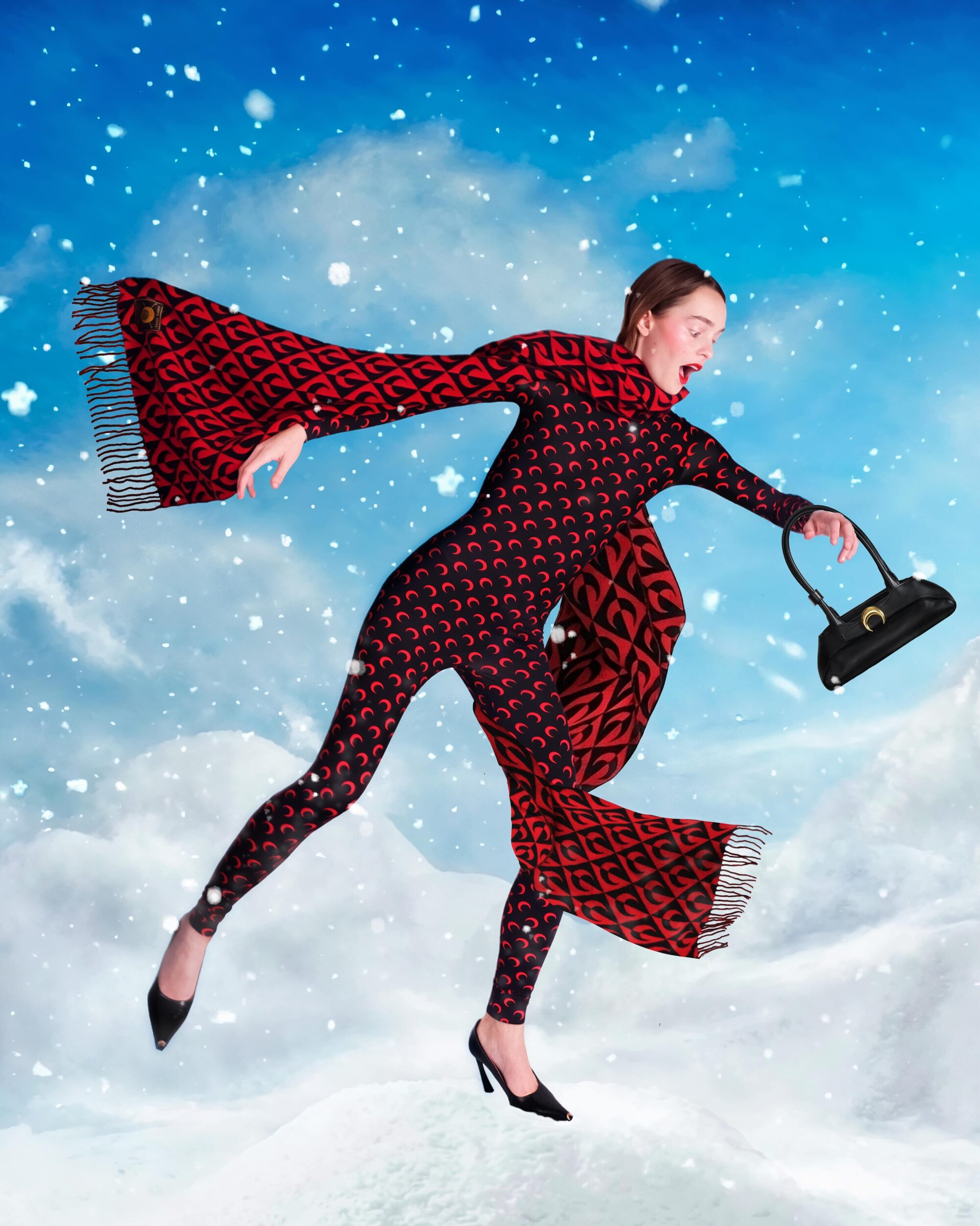 Woman in patterned catsuit and scarf poses in snow-covered landscape with blue sky, holding a black purse and wearing black heels.