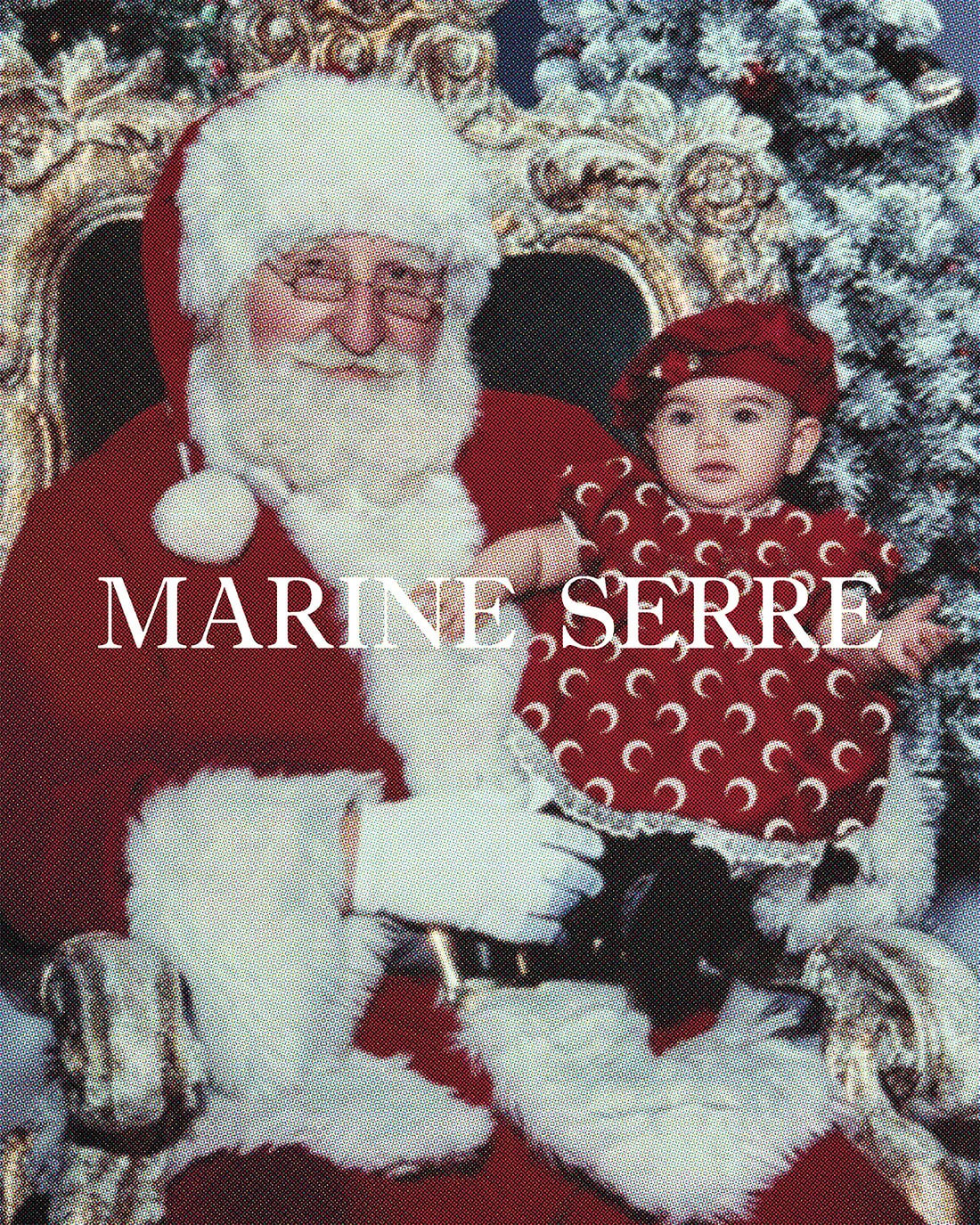 Father Christmas holds a baby wearing a red crescent moon patterned dress and hat, seated in a gilded chair with a Christmas tree backdrop.