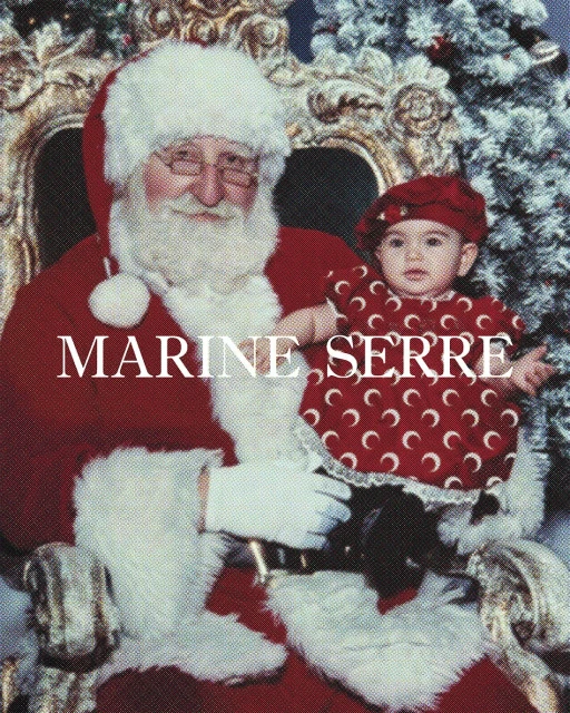 Father Christmas holds a baby wearing a red crescent moon patterned dress and hat, seated in a gilded chair with a Christmas tree backdrop.