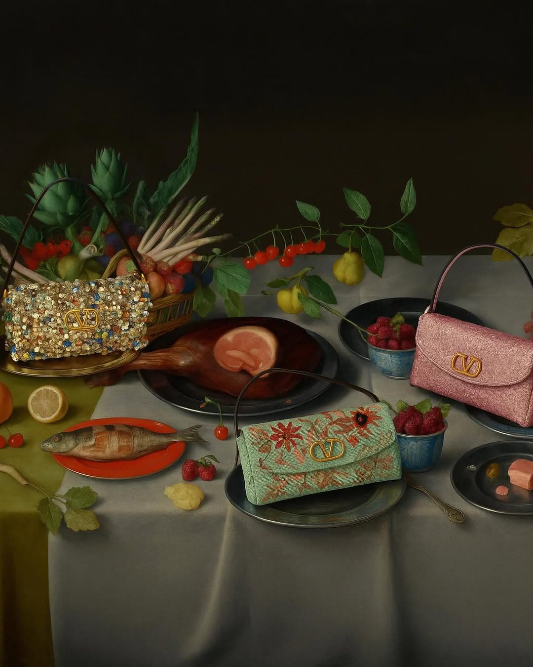 Still life of fashion purses on a draped table with various foods: fish, cherries, berries, meat, and greens on dark background.