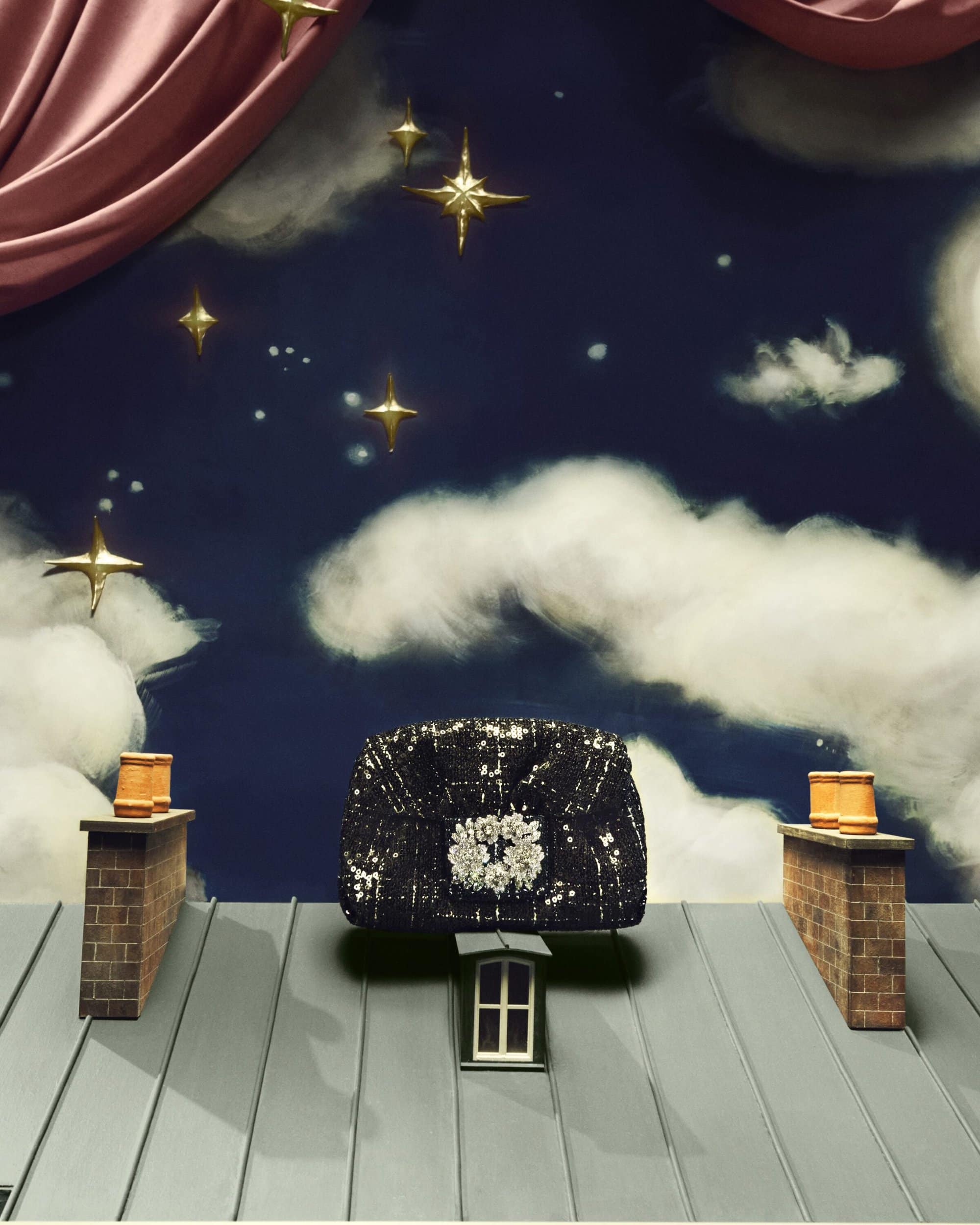A black handbag is centered on a gray roof with brick chimneys and a dark blue sky with clouds and gold star decorations.