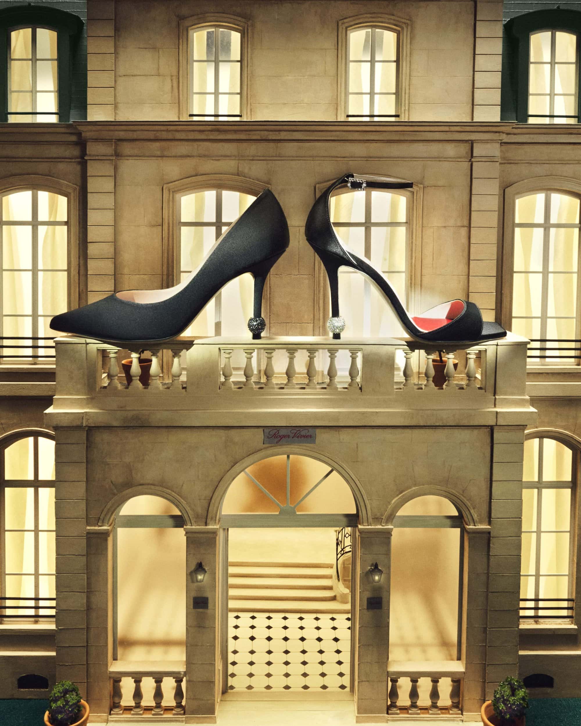 Two black high-heeled shoes displayed on a balcony with a building facade background, evoking a fashion or architecture theme.
