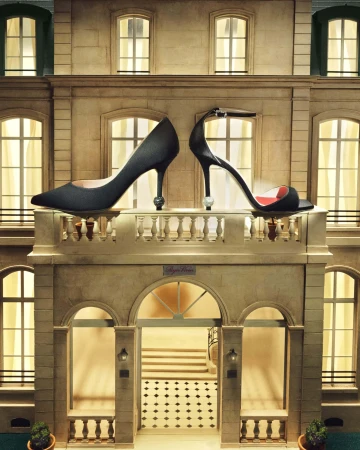 Two black high-heeled shoes displayed on a balcony with a building facade background, evoking a fashion or architecture theme.