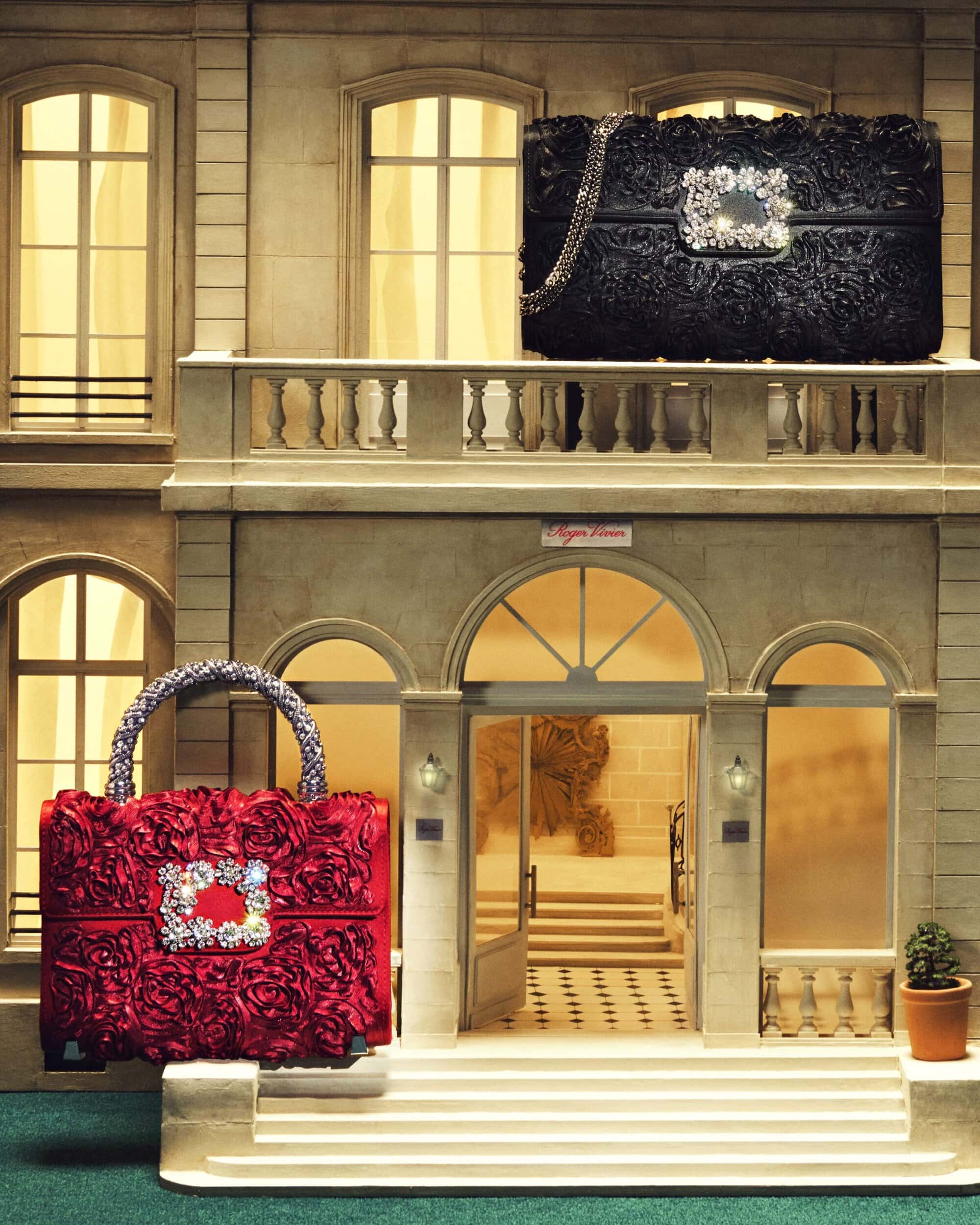 Red and black floral-textured purses with jeweled clasps are displayed in front of a multi-story building exterior with arched entrance.