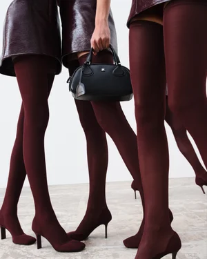 Three models wearing burgundy miniskirts and tights holding a black leather handbag against white background