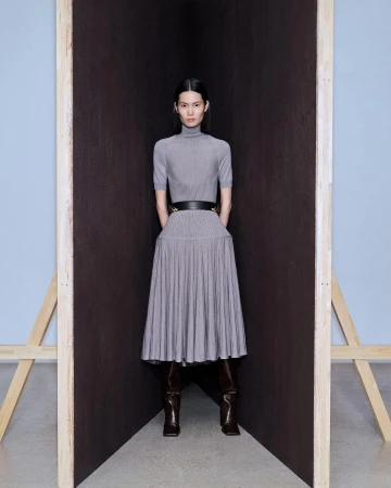 Model wearing a grey turtleneck midi dress and dark boots standing between angled dark panels