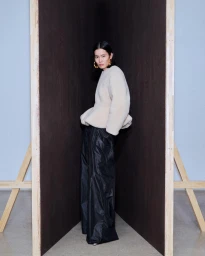 Model standing between dark wooden partition panels wearing a cream textured top and black trousers