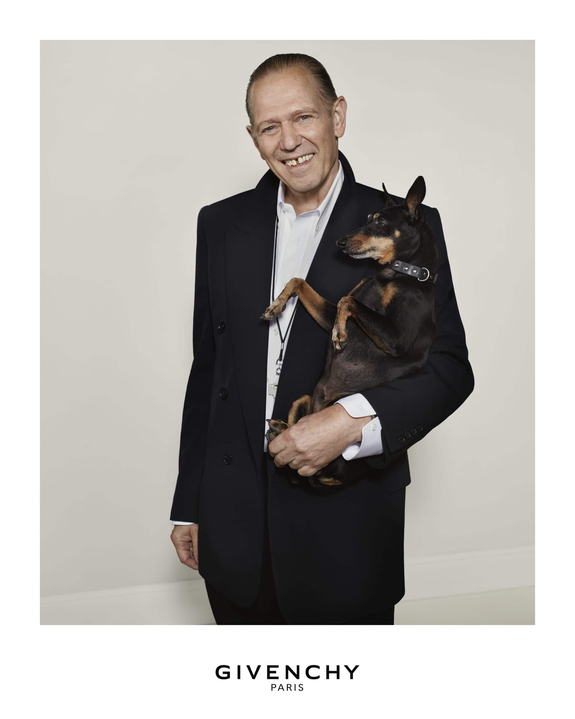 Portrait of an adult man holding a small dog in a photo studio, wearing a black suit jacket and white shirt against a neutral backdrop.