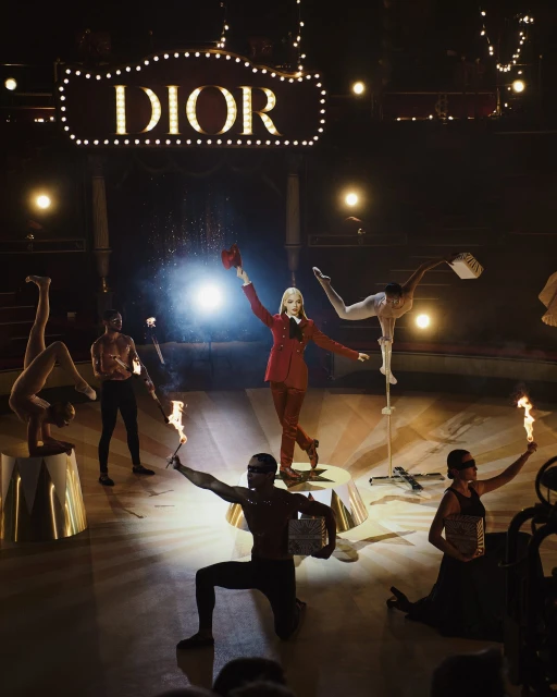 Performance art show with dancers, fire, stage lighting, and a large Dior sign. Fashion, entertainment, and visual spectacle on display.