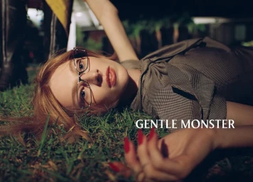 Model Hunter Schafer lying on grass wearing eyeglasses for Gentle Monster Fall 2025 ad campaign.