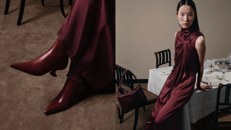 Elegant Asian woman in a draped burgundy dress and burgundy boots posing in an interior with a table and chairs.