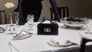 Black velvet handbag with a crystal panther handle resting on a formal white-clothed dining table set with silverware and crystal glassware