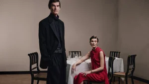 Man standing in dark suit and woman seated in red dress near a dining table in an interior setting for Lanvin.
