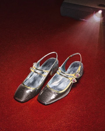Sparkly Mary Jane heels with slingbacks sit on a red background with a projector light shining on the upper right corner.