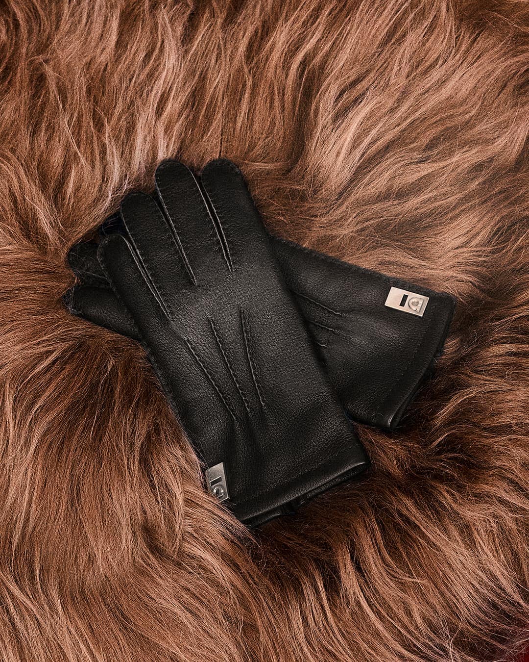 A pair of black leather gloves with metallic hardware resting on a brown fluffy fur texture background.
