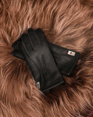 A pair of black leather gloves with metallic hardware resting on a brown fluffy fur texture background.