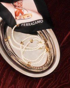 Pearl necklace and black silk scarf with Ferragamo logo arranged neatly on a silver platter over rich red velvet texture.