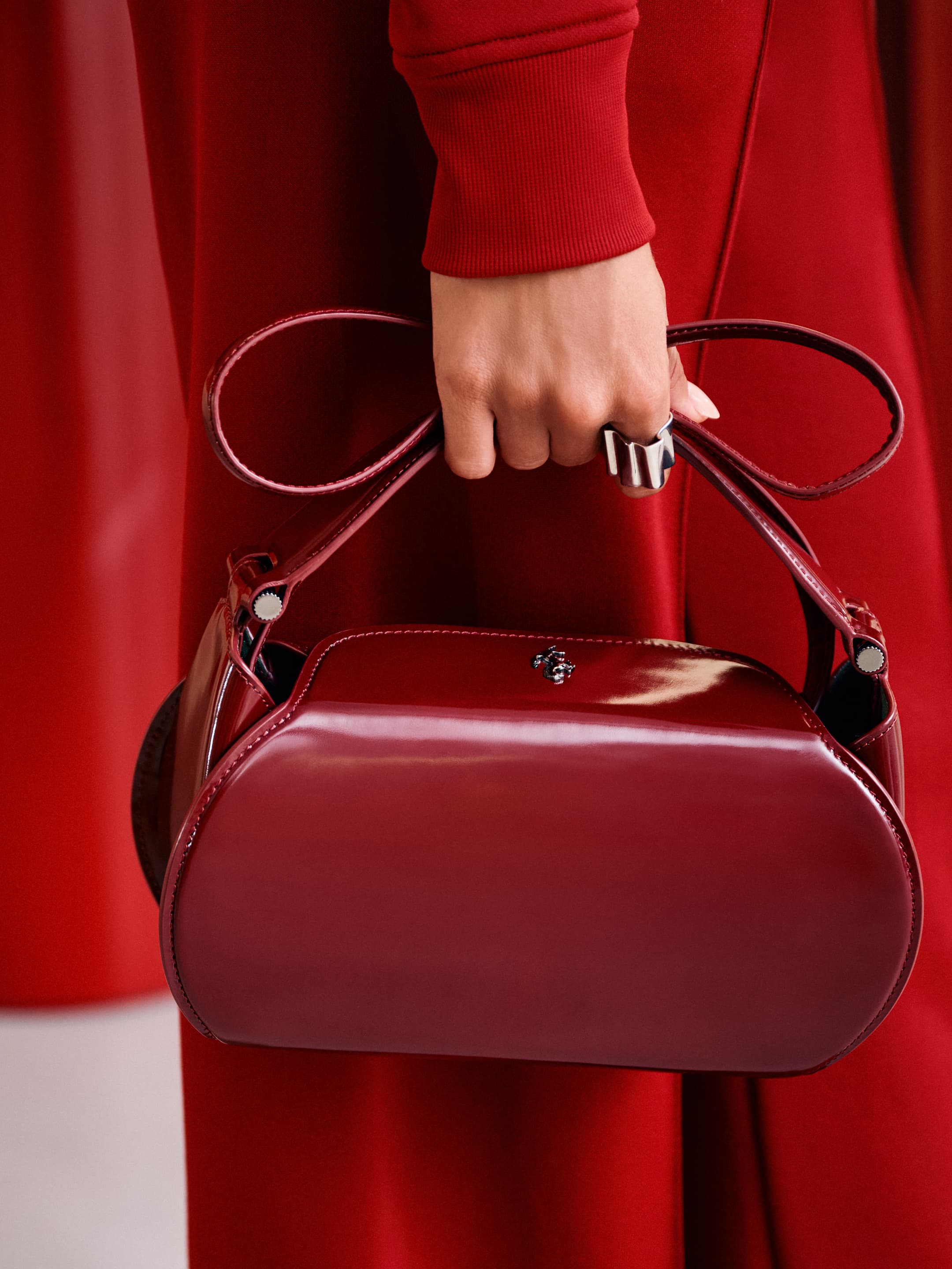 Close-up of an adult female holding a shiny, dark red handbag against a matching monochromatic background, showcasing fashion accessory.