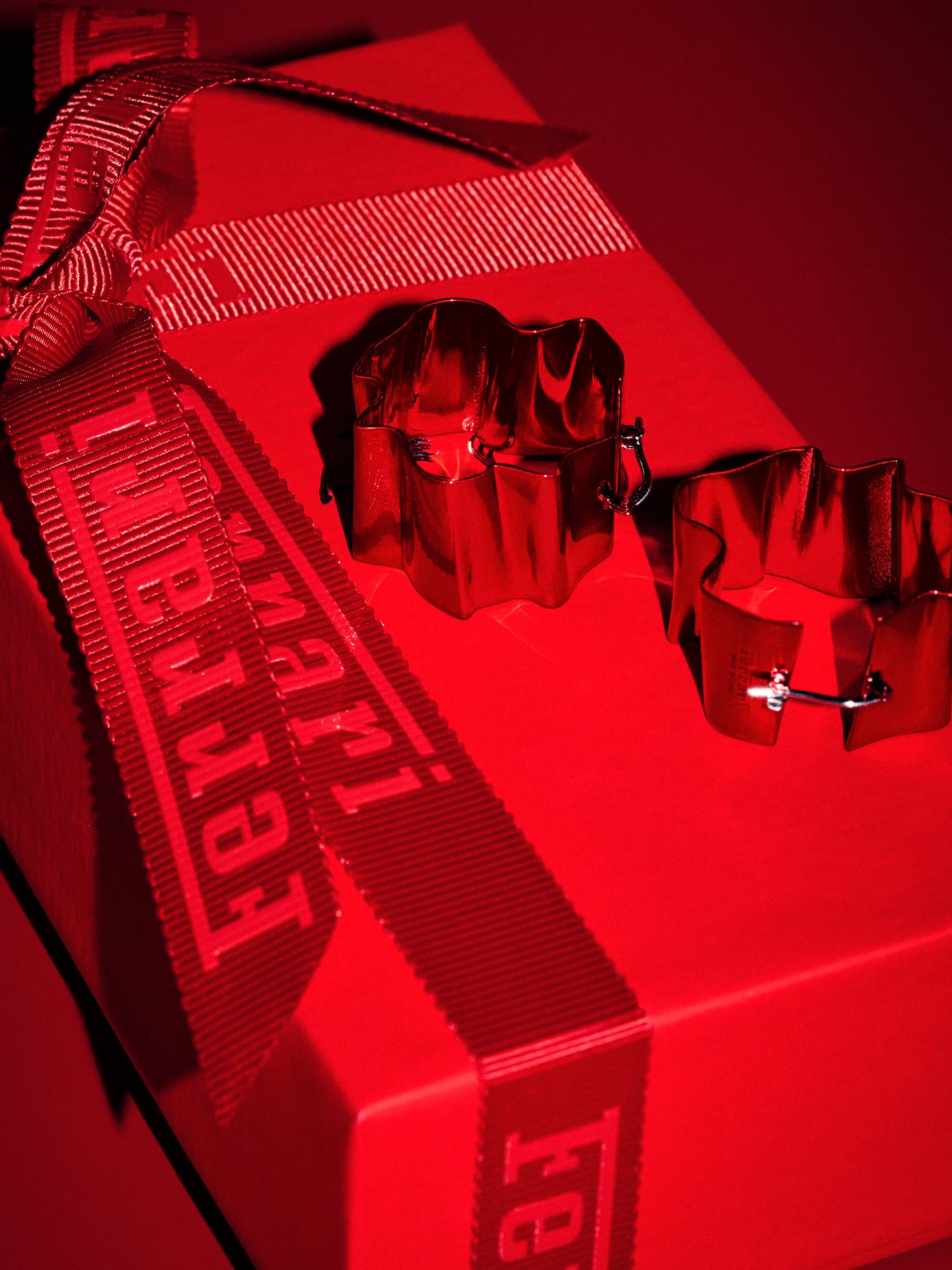 Red gift box with Ferrari branded ribbon and metallic red star-shaped decorations on top, presented against a solid red background.