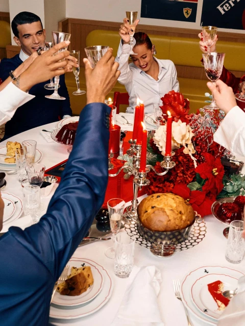 People raise glasses at festive table with red and silver decor, enjoying a panettone cake under warm indoor lighting.
