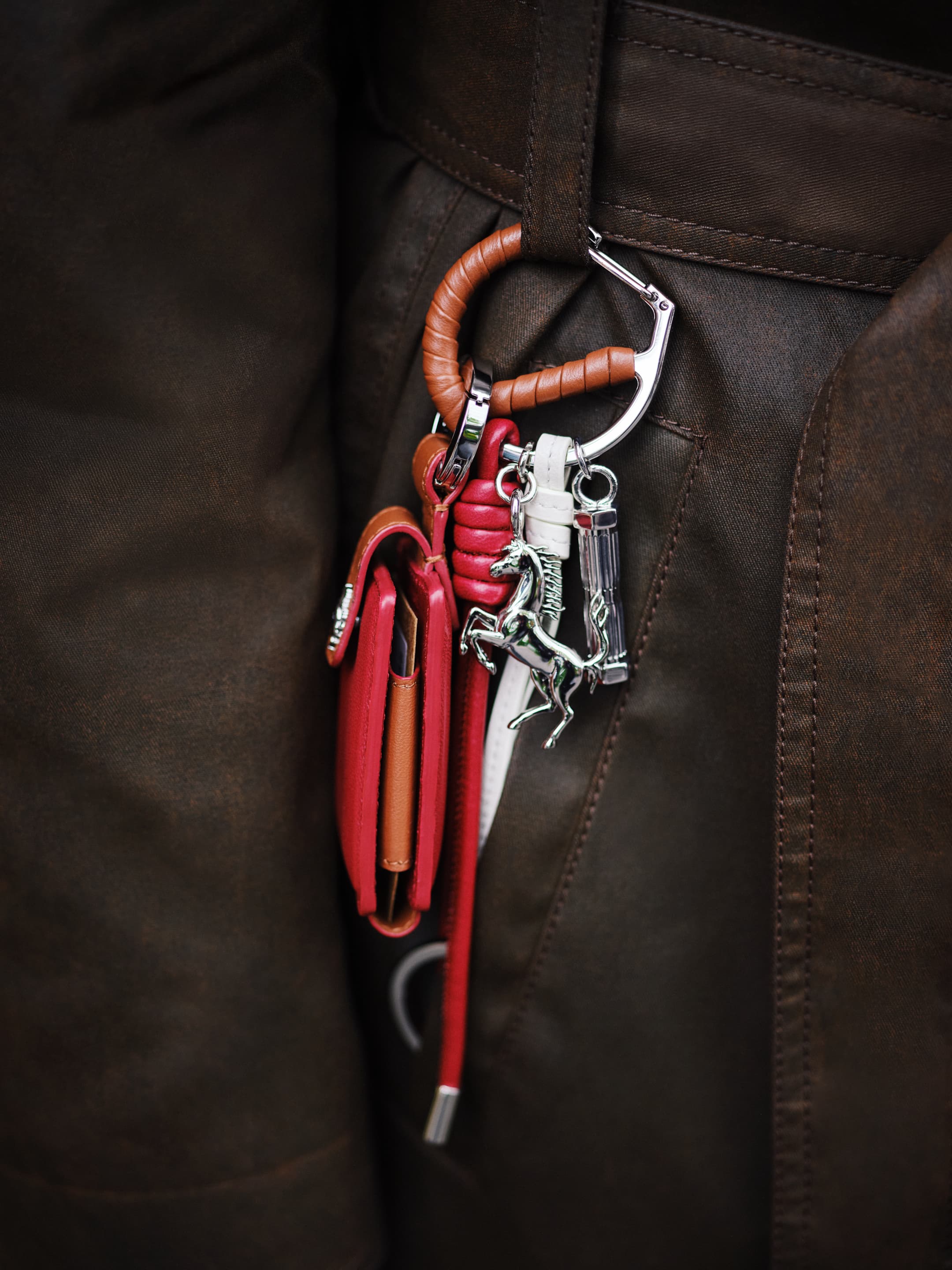 Close-up of a brown leather jacket with a wallet, carabiner, and charms hanging from a belt loop, fashion detail.