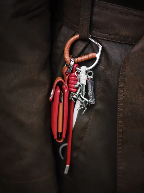 Close-up of a brown leather jacket with a wallet, carabiner, and charms hanging from a belt loop, fashion detail.